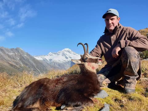 Hunter with a chamois under a clear blue sky, snowy mountain behind