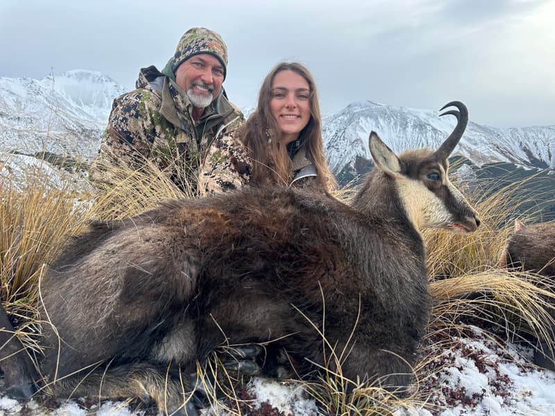 Two hunters with an alpine chamois in front of snow-covered peaks