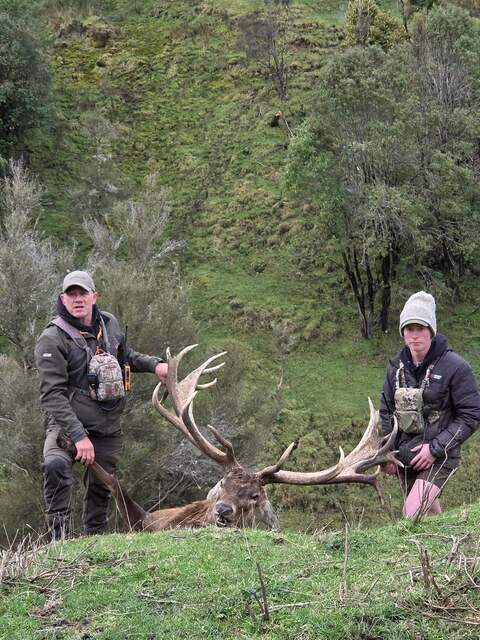 Two hunters with a red stag in a steep green gully