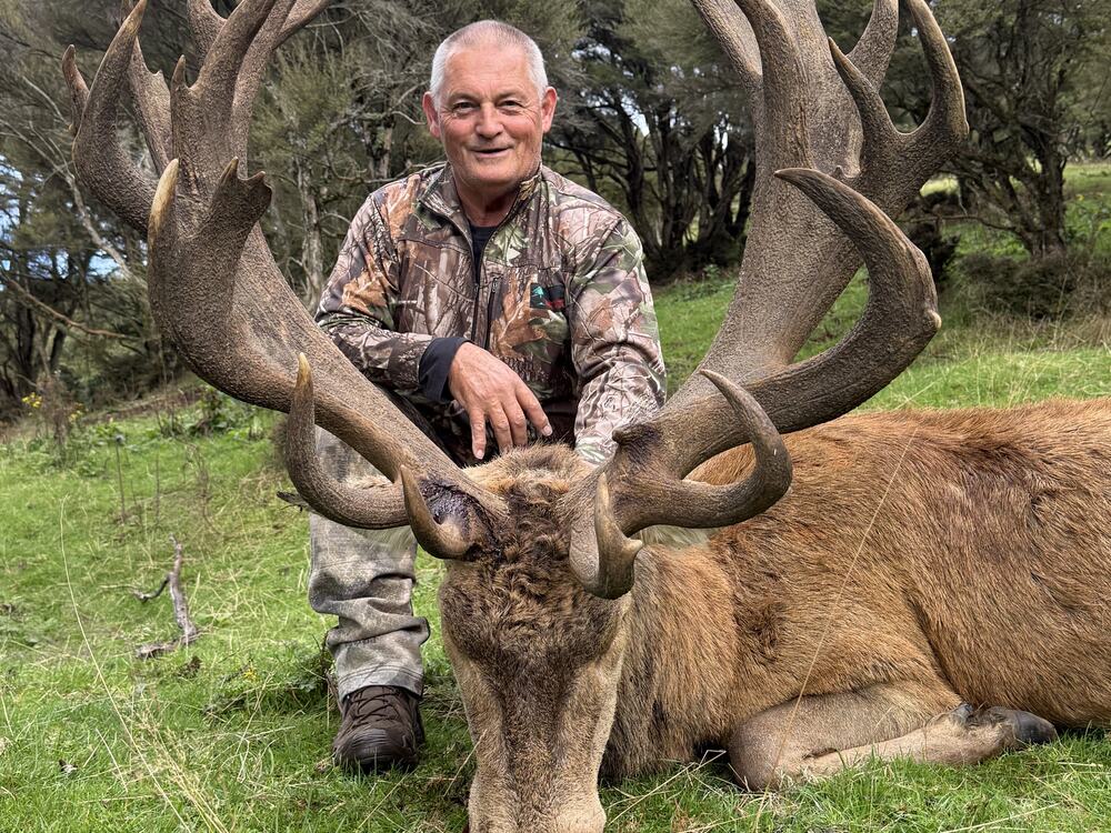 Hunter with a heavy-antlered red stag trophy in private hill country