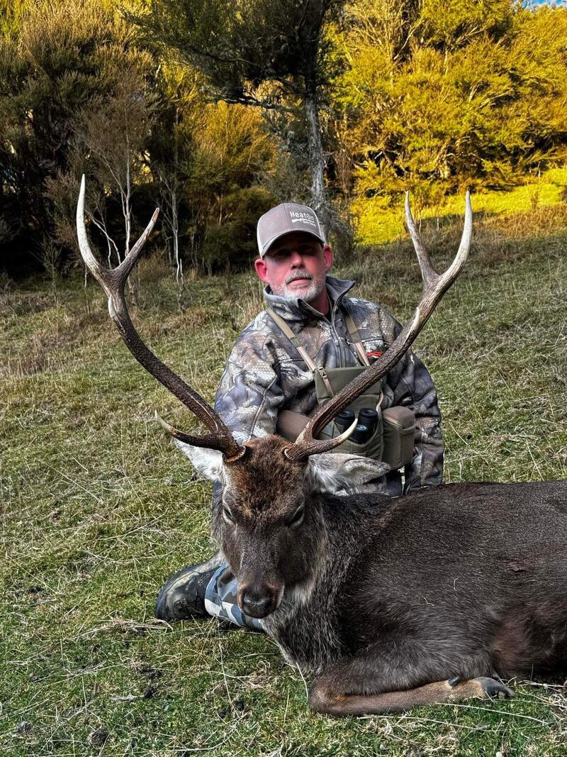 Hunter with a sika stag against golden autumn bush